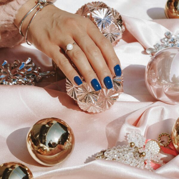 Stylish hand showcasing blue nails resting on pink satin surrounded by opulent ornaments and jewelry.